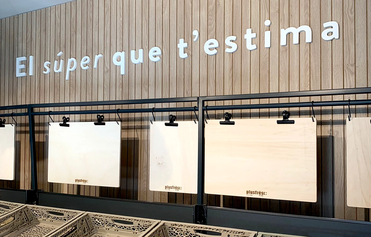 Eslógan letras corpóreas en blanco sobre pared revestida de madera supermercado PlusFresc
